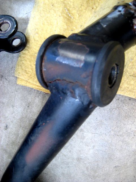 1996 Ford Bronco - Close-up of a worn and cracked black suspension bushing on a metal component, likely needing replacement.