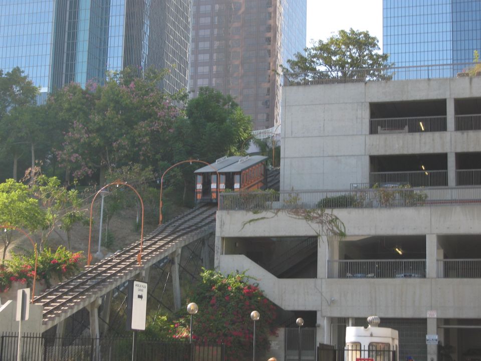 Two wooden funicular cars on tracks ascending a hill, with modern buildings in the background