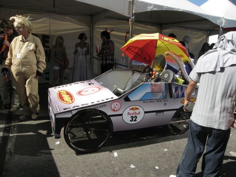 1986 Ford Bronco - A custom-built soap box derby car with Red Bull logos and an umbrella is displayed at an event.