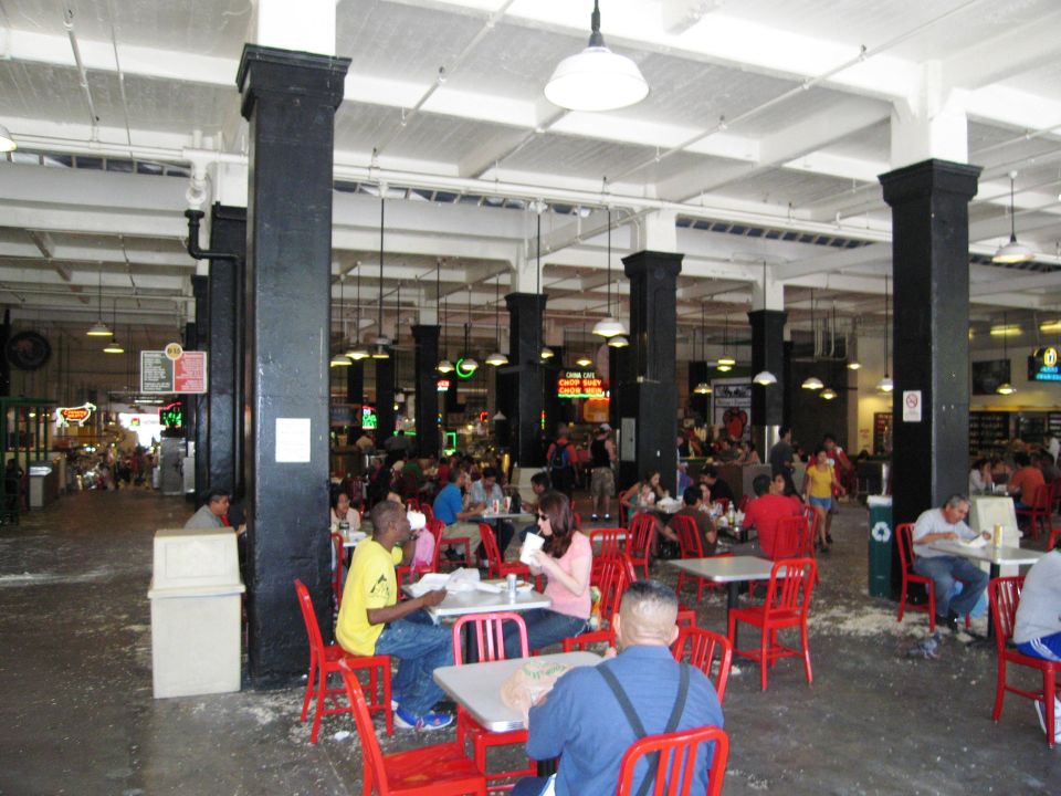People eating at tables in a busy indoor market with black columns and white ceiling