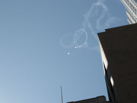 1986 Ford Bronco - Two planes create smoke rings in the sky above city buildings during an airshow.