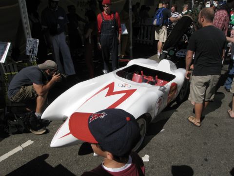 1986 Ford Bronco - A white car with a red M emblem is displayed outdoors with spectators and a photographer nearby.