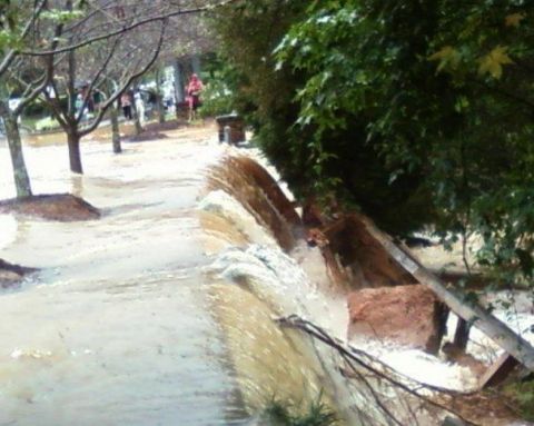1979 Ford F-150 - A scene of flooding with water flowing over a retaining wall, with trees and people visible in the distance.