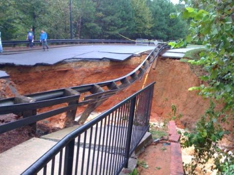 1979 Ford F-150 - A road has collapsed, revealing a large sinkhole and eroded embankment, with guardrails hanging precariously.