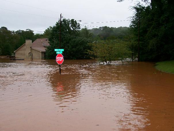 Flooded street with a stop sign and a house partially submerged in brown water