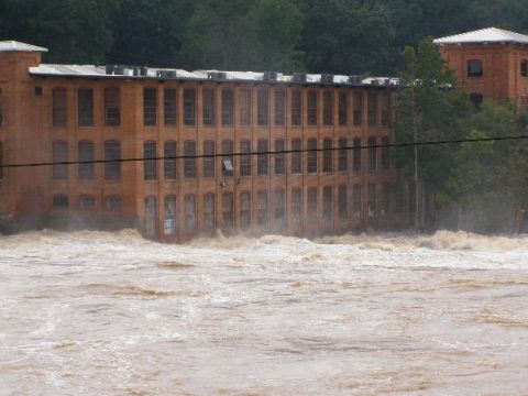 1979 Ford F-150 - A river has flooded its banks, inundating the area in front of a historic brick industrial building.