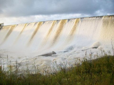 1979 Ford F-150 - A large dam is overflowing with water cascading down its face, creating a powerful scene under a dramatic sky.