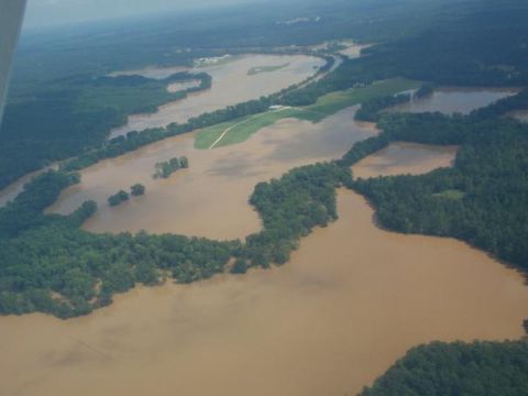 1979 Ford F-150 - An aerial perspective captures a vast expanse of land submerged under muddy floodwaters, with trees and green fields partially visible.