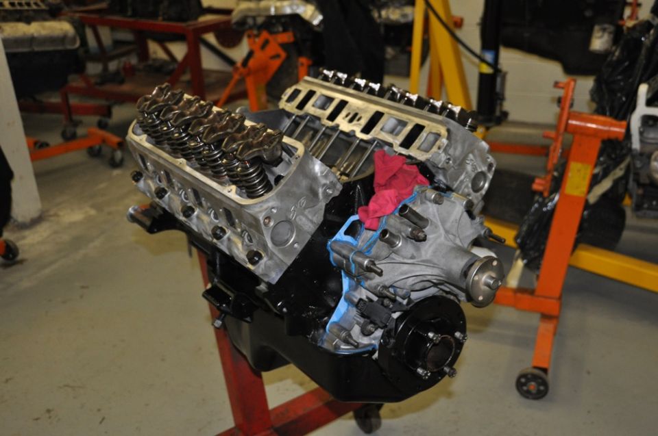 V8 engine block on a stand, with valve covers removed showing internal components. A red rag is placed on top