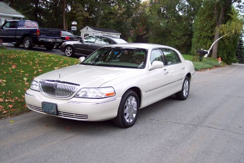 2001 Ford Crown Victoria - A white 2001 Lincoln Town Car is parked on a residential street, with other vehicles visible in the background.
