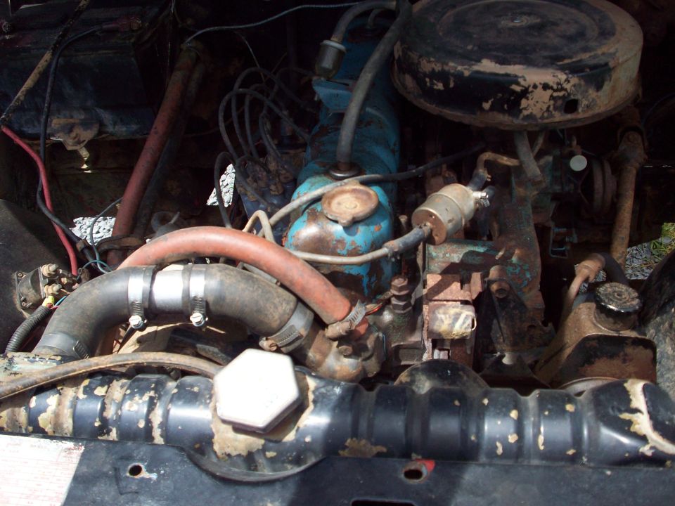 Engine bay of a 1968 Jeep CJ5 showing blue inline engine, round air cleaner, red radiator hose, and rusty components
