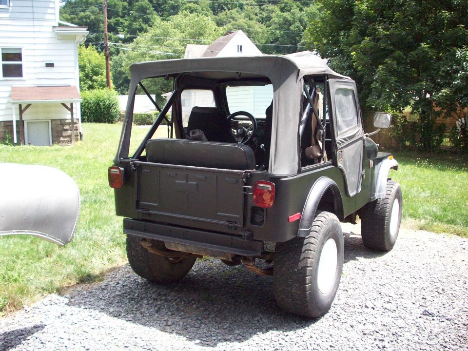 Rear view of black Jeep CJ5 with soft top and large off-road tires on gravel driveway