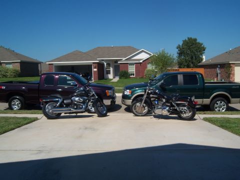 1996 Ford Bronco - Two motorcycles are parked in front of two pickup trucks in a suburban driveway.