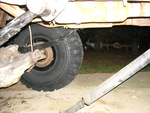 1979 Ford F-150 - The underside of a truck shows its rear axle, suspension components, and a large off-road tire, with another vehicle's axle in the backgrou…