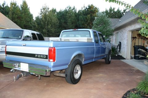 1995 Ford Bronco - A blue Ford F-Series pickup truck is parked in a driveway next to a silver SUV, with a brick house and garage in the background.
