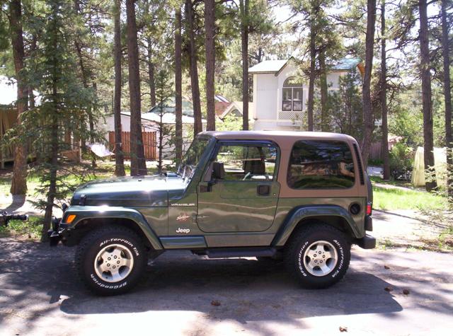 Green 2002 Jeep TJ Wrangler with a brown soft top, parked on a dirt road