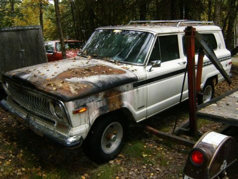2000 Ford E350 - A weathered white Jeep Grand Wagoneer sits in an outdoor setting, partially obscured by trees and a wooden structure.