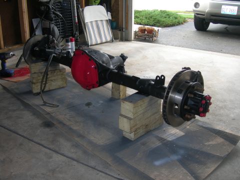 1991 Jeep Wrangler - Rear axle assembly with red differential cover and disc brakes, resting on wooden blocks in a garage.