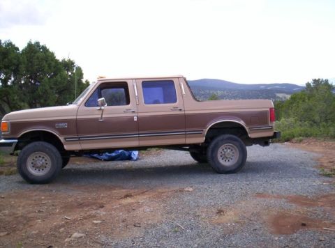 1988 Ford C-350 (Centurion Conversions) - This extended cab pickup truck is parked on a gravel surface with hills and trees in the background.