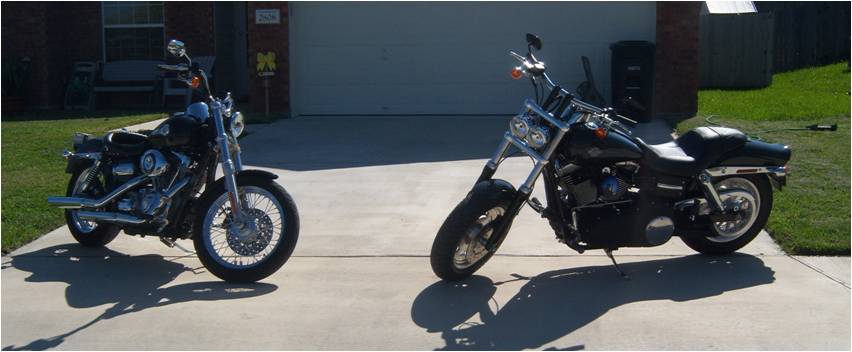 Two black motorcycles parked in front of a garage. One is closer and to the right, the other is further back and to the left
