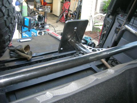 1996 Ford Bronco - A fabrication in progress inside a stripped vehicle, with a welded steel tube and a bolt-in plate mount running across the bare floor pan.…