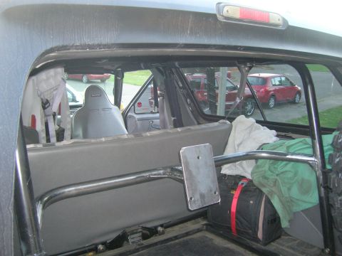 1996 Ford Bronco - The interior of a vehicle is shown, a roll cage and racing seats, with other vehicles visible outside.