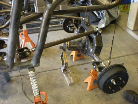 Suzuki Samurai - In-progress tube-chassis buggy build on orange jack stands in a garage, with the bare bent-tube frame sitting above a fabricated link suspe…