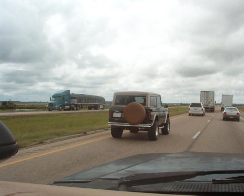 1975 Ford Bronco - A 1975 Ford Bronco is seen from behind on a highway, with other vehicles and a truck in the distance.