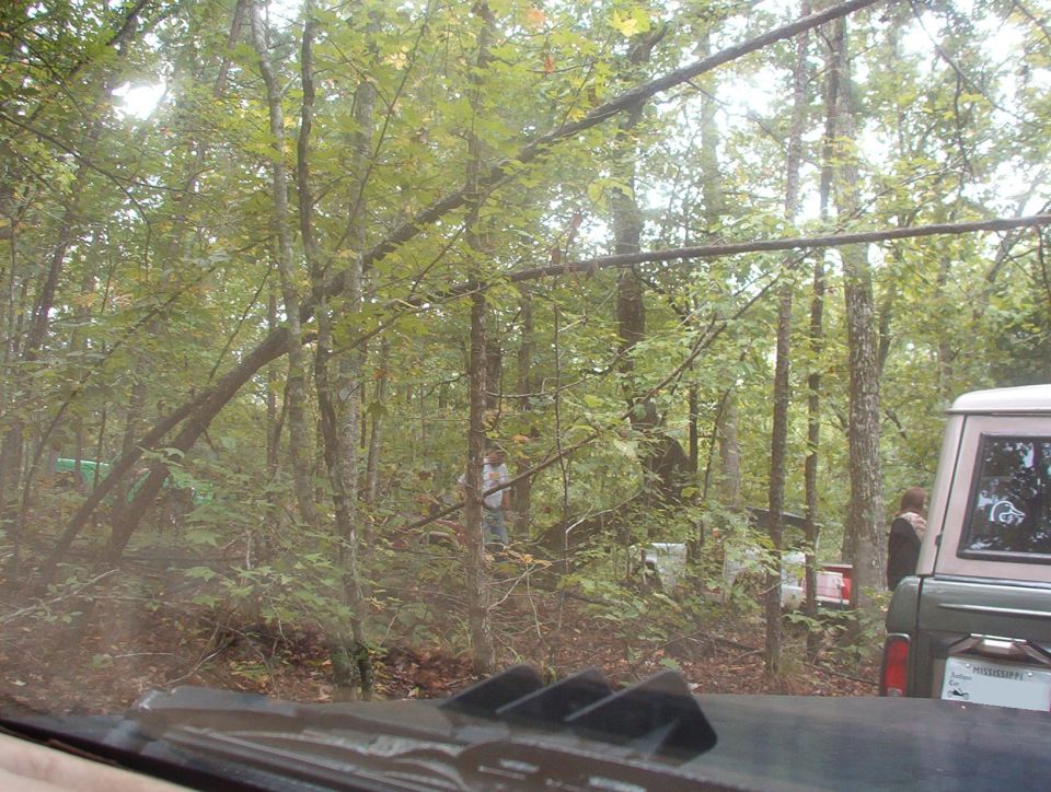 View through a windshield of wooded off-road trail with vehicles among trees