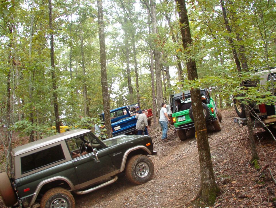 Group of off-road SUVs including a green early Bronco gathered on a forest trail