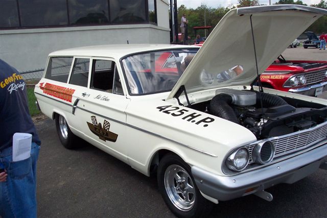 White 1961 Ford Falcon wagon with hood open, showing engine. "425 H.P." on hood. Another red car behind it