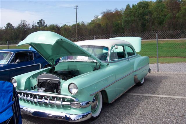 Mint green and white two-door sedan with hood and trunk open. Another car is parked to the left