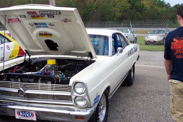 1969 Ford Fairlane, white, hood open showing engine, NHRA license plate. Other cars and person visible