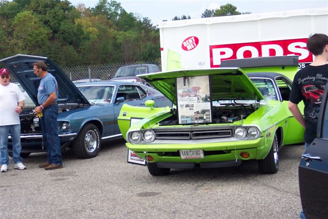 Lime green muscle car with hood open, showing engine and display board. License plate reads VANISHING