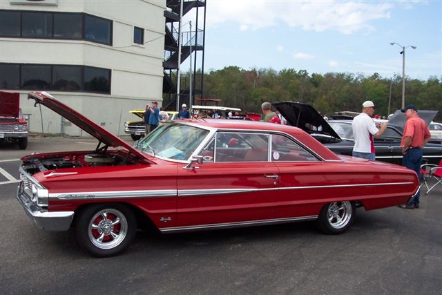 Red 1963 Ford Galaxie 500XL coupe with hood open, parked at an outdoor car show