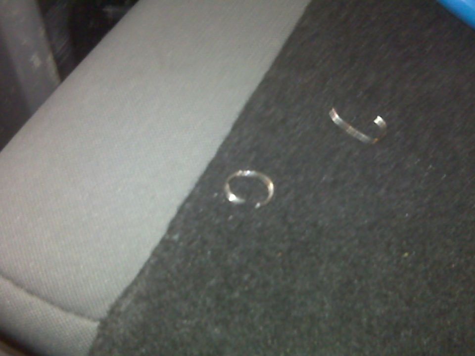 Two metal clips on a dark fabric surface, possibly a car seat