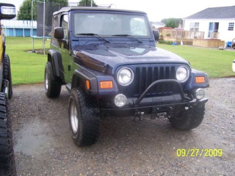 2003 Jeep Wrangler - A dark blue 2003 Jeep Wrangler is parked outside on a gravel driveway with a backyard visible in the background.