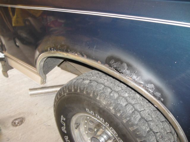 Rust and blistered paint on rear wheel arch of dark blue Bronco, with primer sprayed over the fender lip