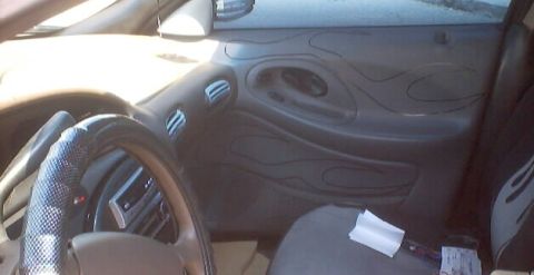 1999 Ford Taurus - Interior view of a car's driver side door panel with custom flame graphics and a covered steering wheel.