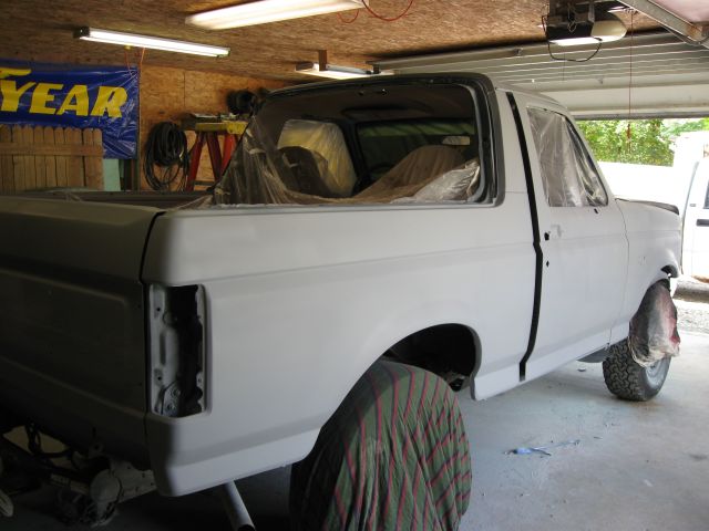 Ford pickup bed and cab in primer being prepped for paint in a garage