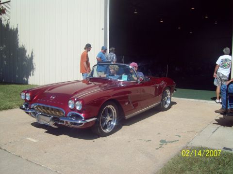 1995 Ford Probe - A classic red Chevrolet Corvette convertible is displayed outdoors with people around.