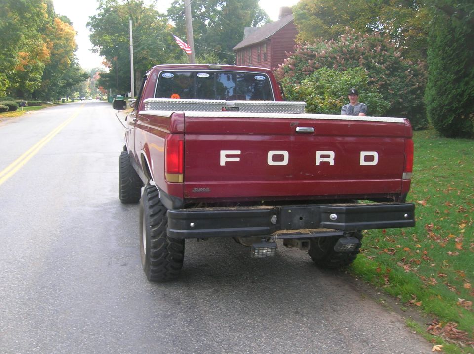 Rear view of a red Ford pickup truck with a toolbox in the bed and large tires