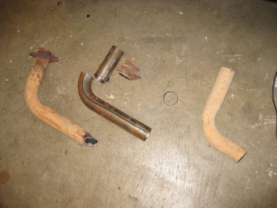 Rusty exhaust downpipe and freshly bent bare steel replacement pipe sections on shop floor