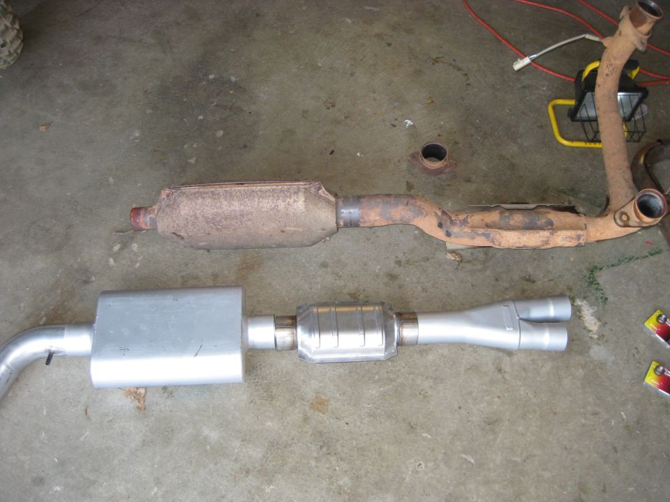 Old rusty exhaust pipe and catalytic converter next to a new muffler and dual exhaust tips