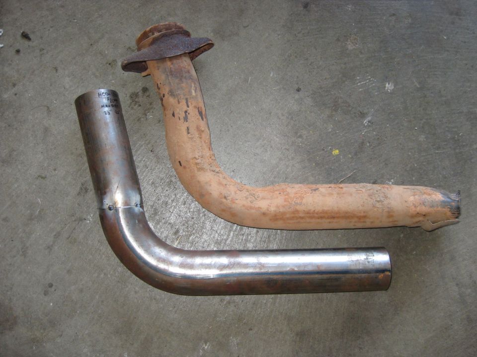 Two exhaust pipes, one new and shiny, the other old and rusted, lie on a concrete surface