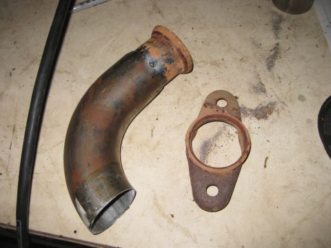 1995 Ford Bronco - A rusty exhaust pipe and a separate flange sit on a workbench, likely for a Y-pipe build.