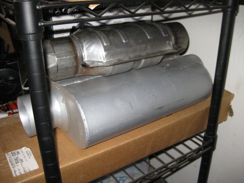 1995 Ford Bronco - Exhaust system parts, including a catalytic converter, are stored on a metal shelf.