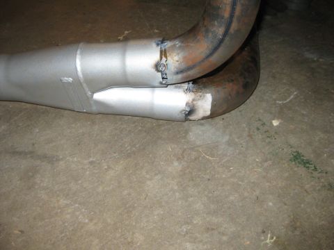1995 Ford Bronco - A silver-painted dual exhaust Y-pipe assembly lying on a concrete floor, with tack welds joining new slip-fit tubing to rusty, heat-scaled…