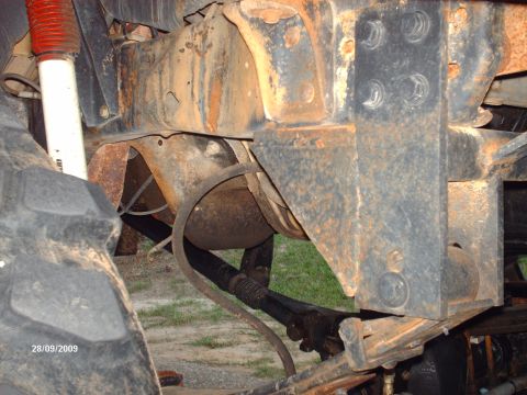 1990 Ford F-150 - The underside of a heavily rusted truck shows its frame, suspension, and driveshaft components.