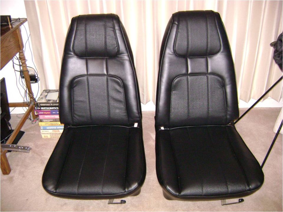 Pair of reupholstered black vinyl bucket seats on carpet in front of curtains